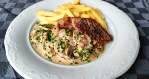Šťavnatá vepřová krkovice s krémovou žampionovou omáčkou a hranolky na talíři